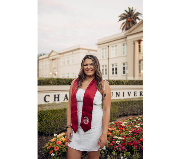 Allysha Proulx-Walter at Chapman University in a white dress and her honors stole on her shoulders